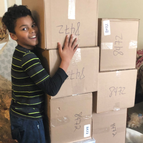 A boy hugging the boxes he recieved for Christams from Holiday Helpers Canada